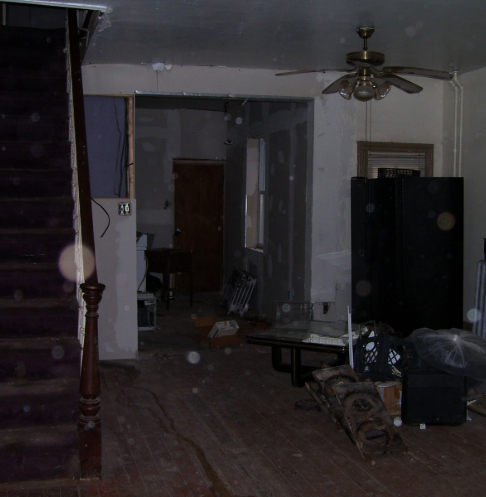 Cluttered and unfinished room with exposed walls, a staircase, and various pieces of furniture and debris scattered throughout.